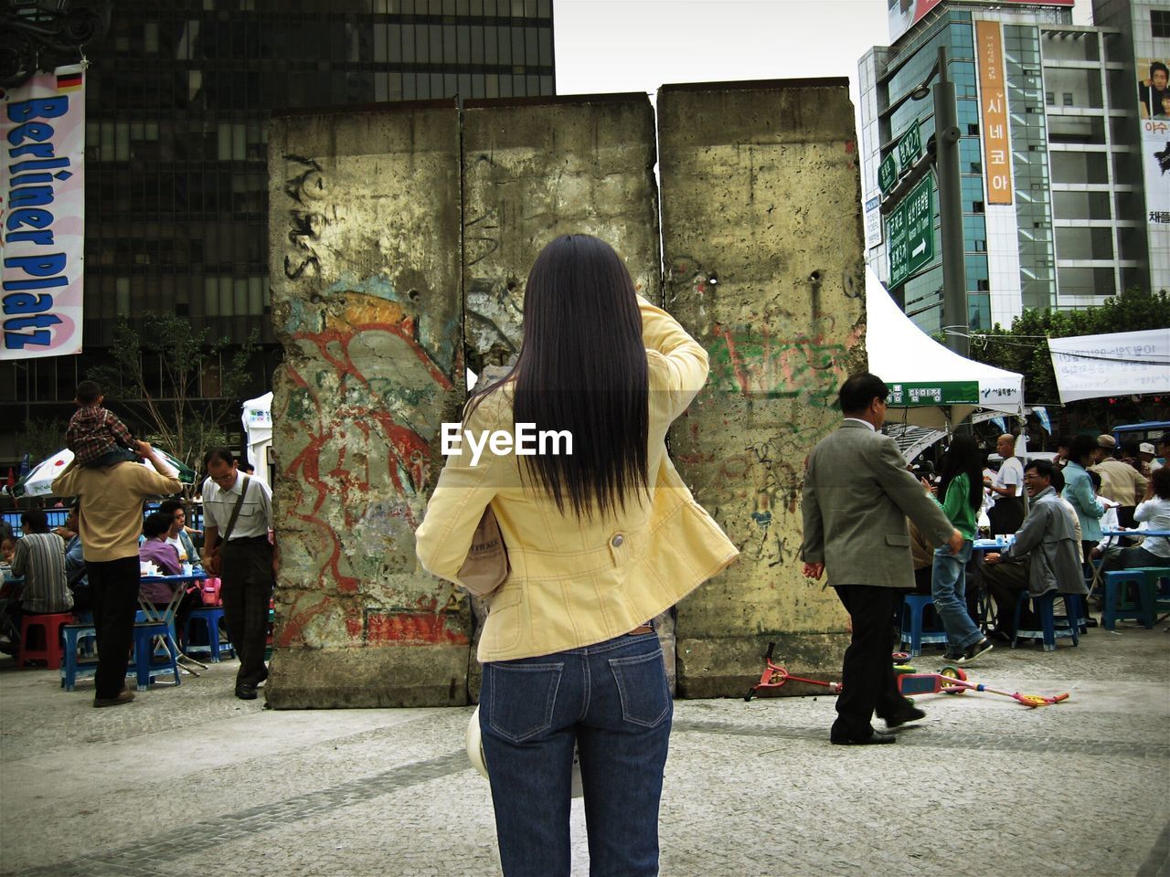 Rear view of woman standing on footpath against berlin wall