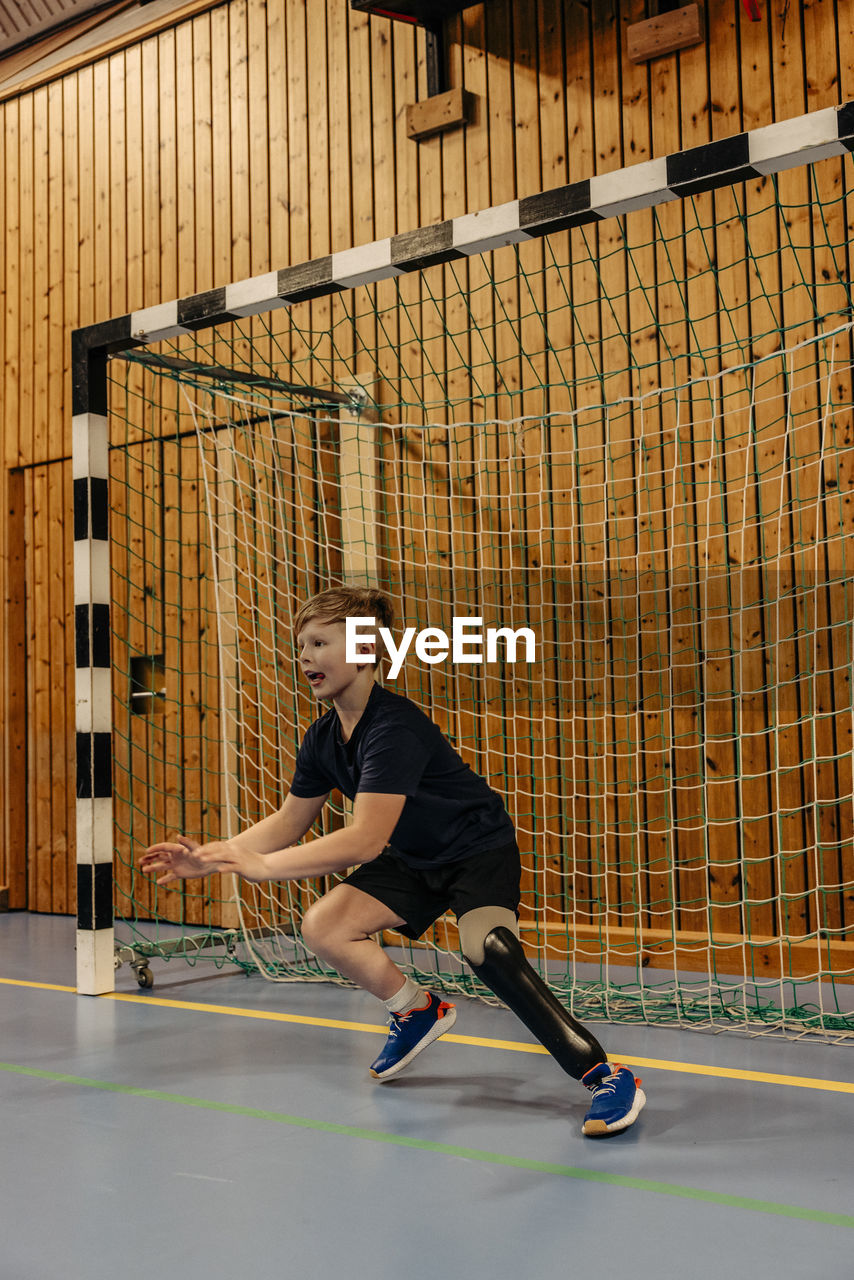 Boy with disability goalkeeping near net while playing football at sports court