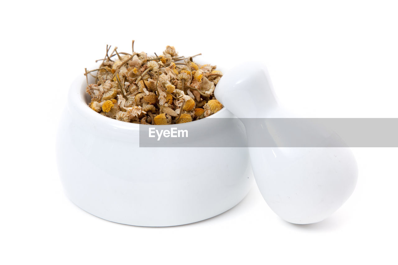 Close-up of dried chamomile in mortar with pestle on white background