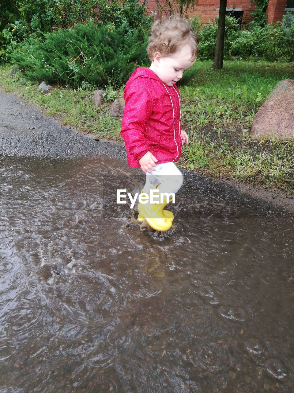 Cute girl wearing raincoat while playing in puddle on footpath