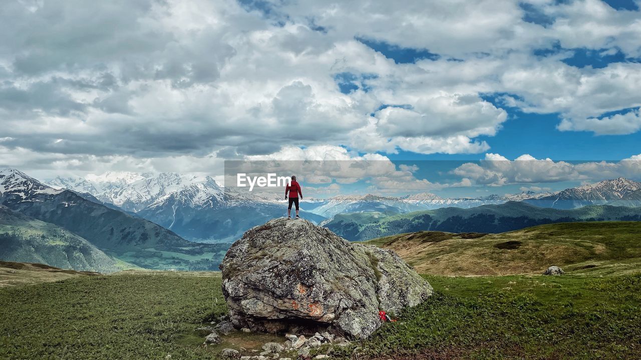 REAR VIEW OF MAN STANDING ON MOUNTAIN