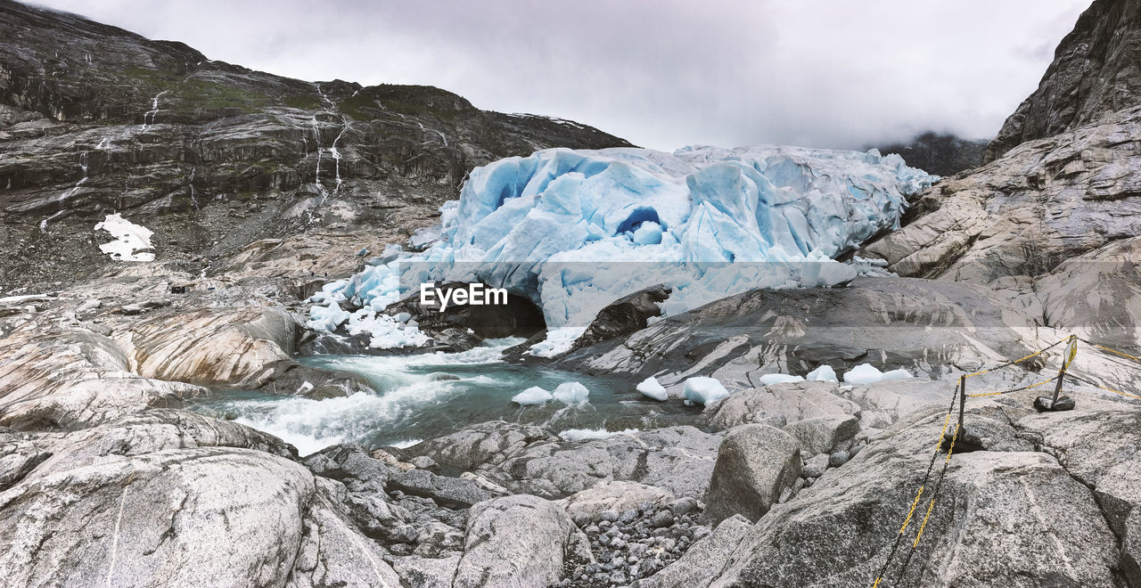 Scenic view of glacier on rocks by waterfall against sky