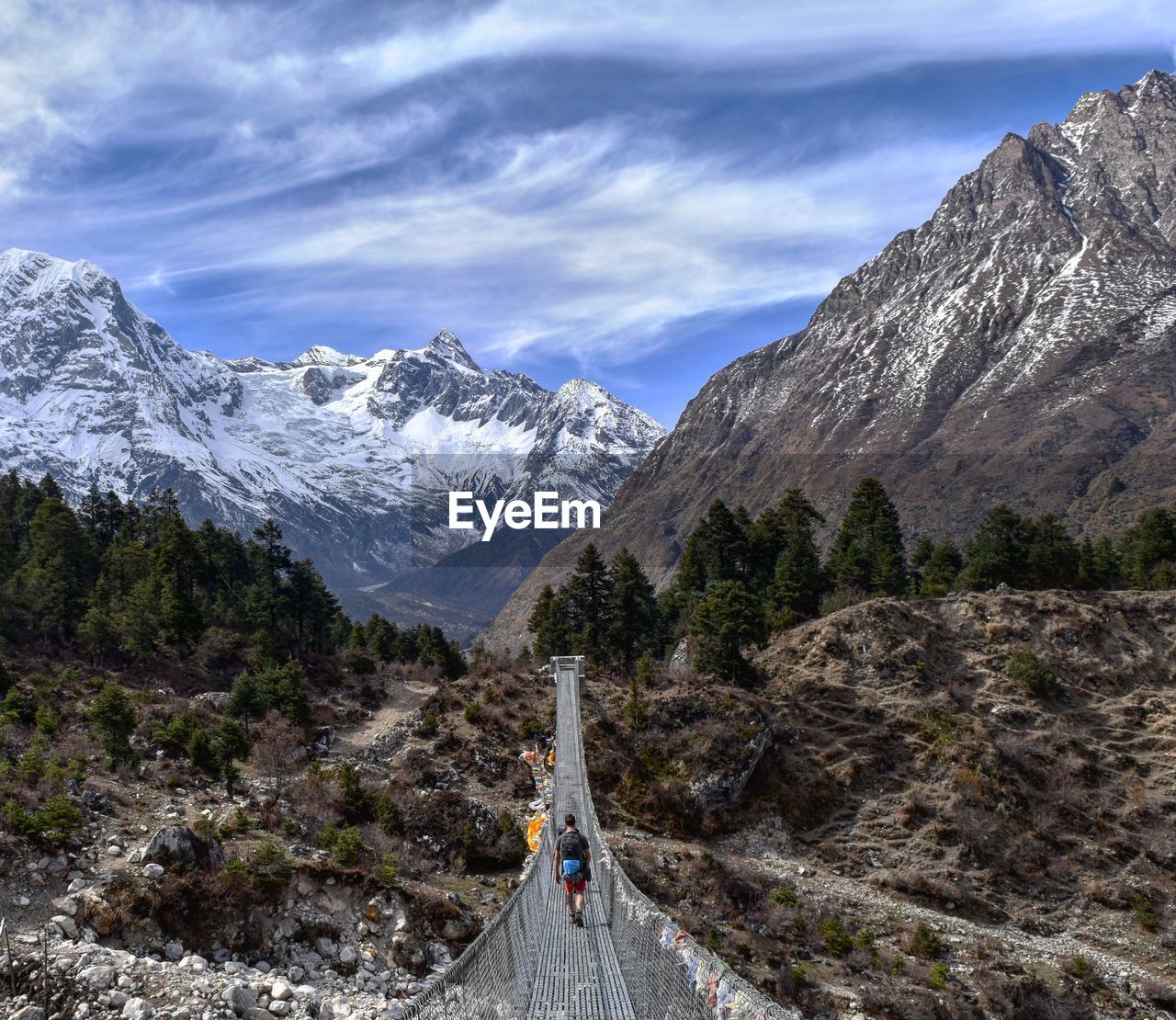 Tourists on suspension bridge against snow covered mountain