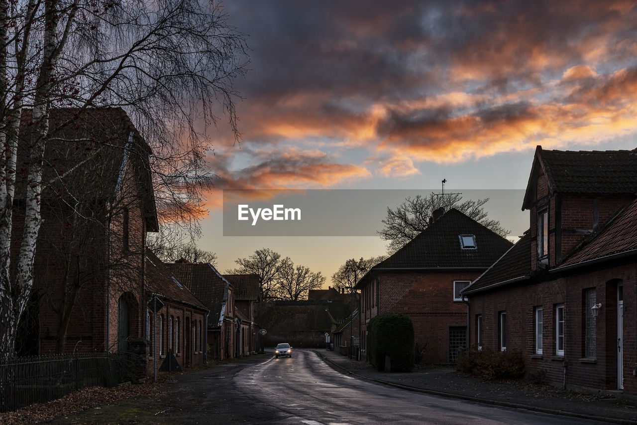 EMPTY ROAD AMIDST BUILDINGS AND TREES AGAINST SKY