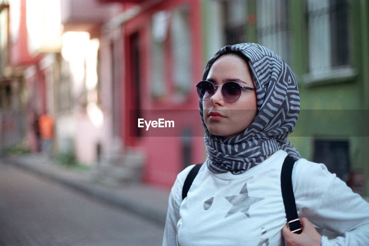 Woman wearing sunglasses and scarf standing against building