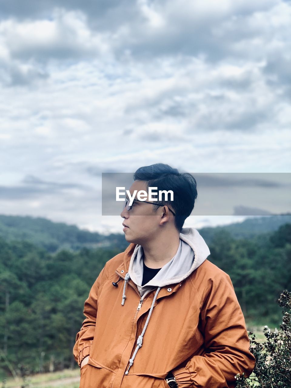 Young man looking away while standing on mountain against sky