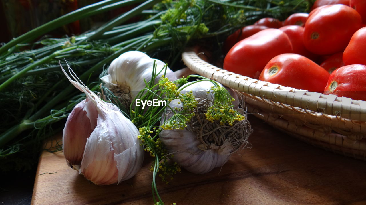 Close-up of tomatoes in bowl by garlic bulbs and herbs on table