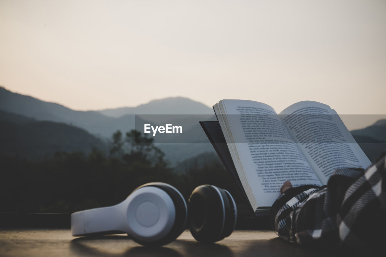 CLOSE-UP OF OPEN BOOK AGAINST SKY DURING SUNSET