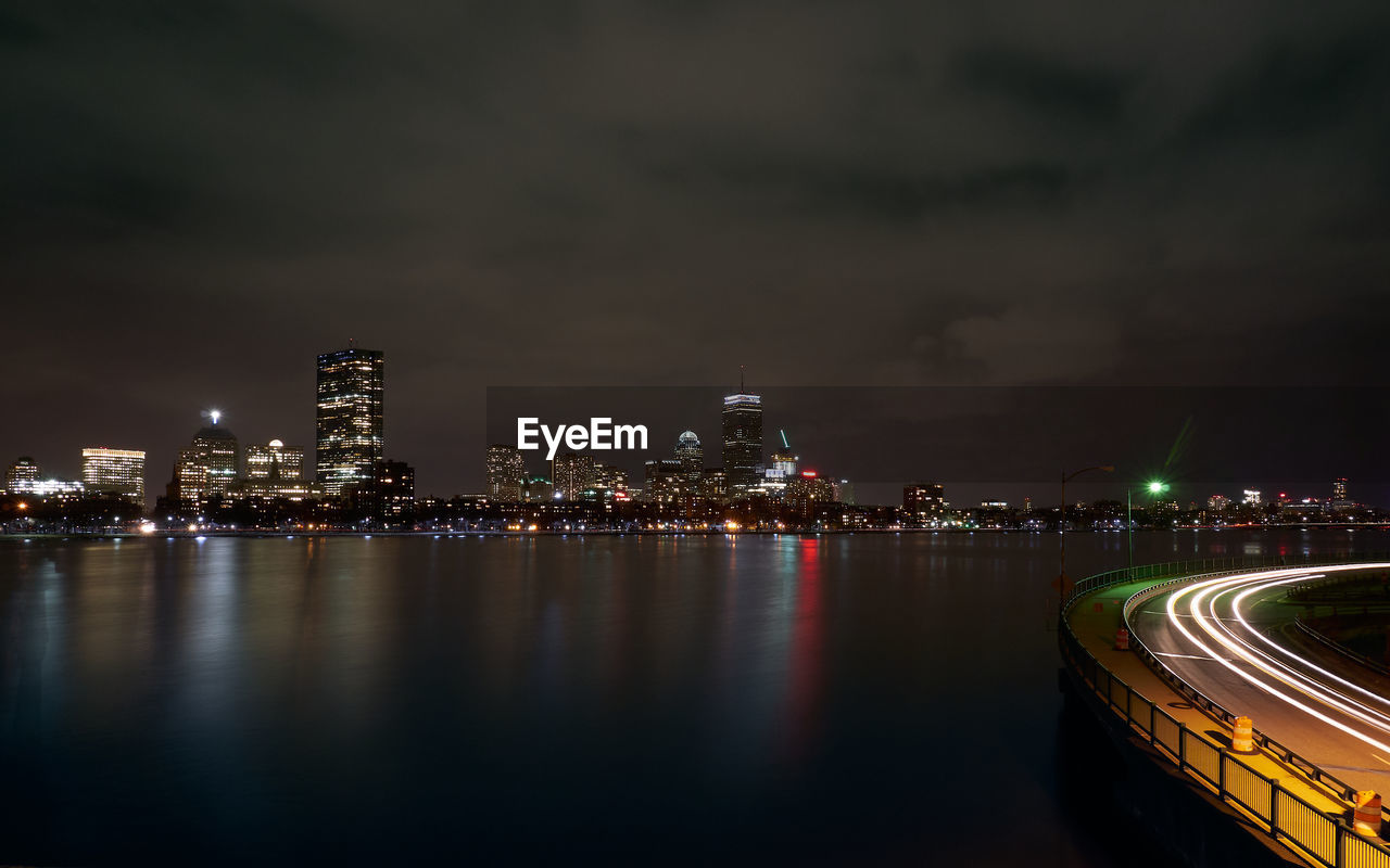 Illuminated buildings by river against sky at night