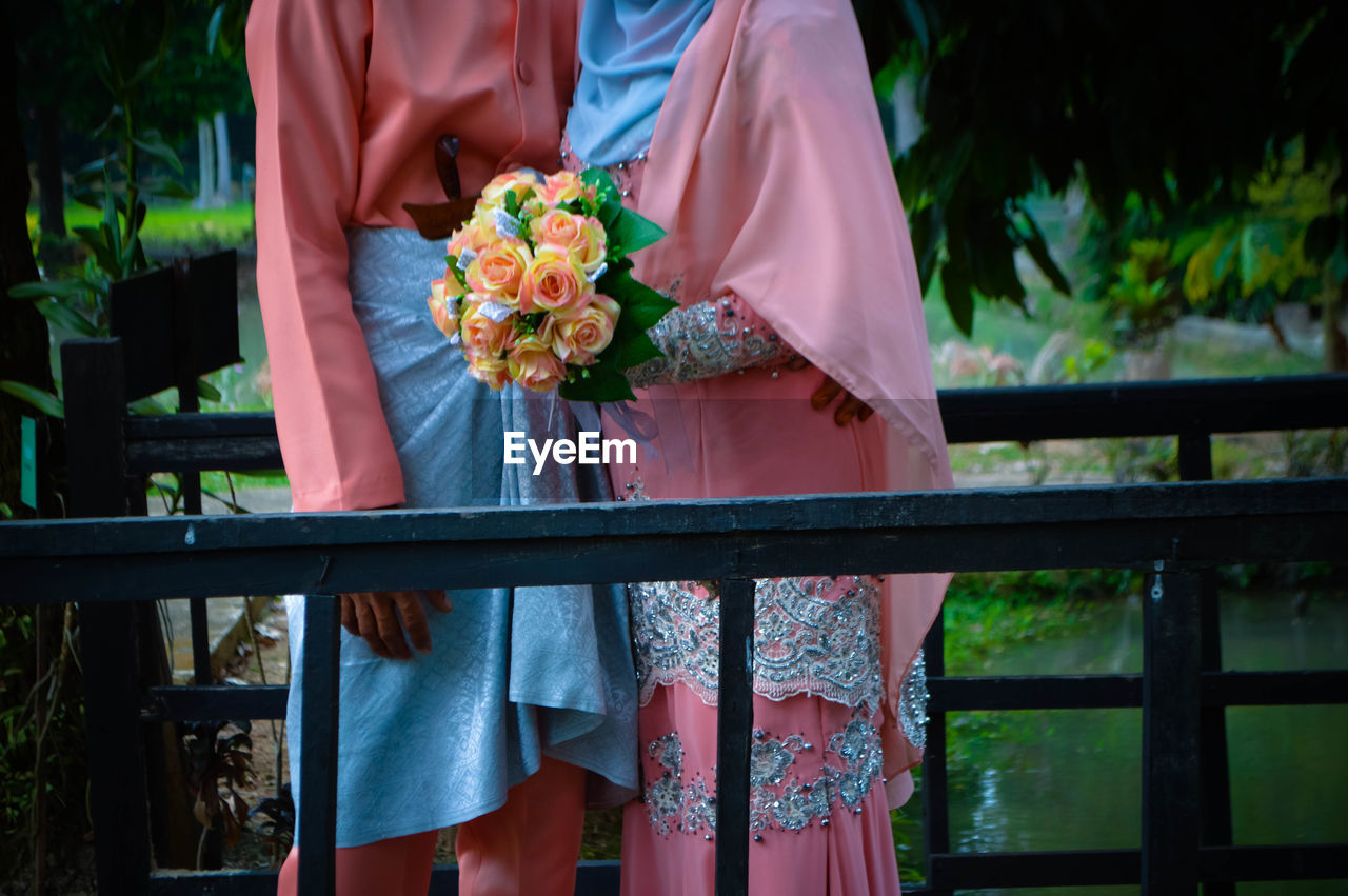 Midsection of bride and groom standing on bridge