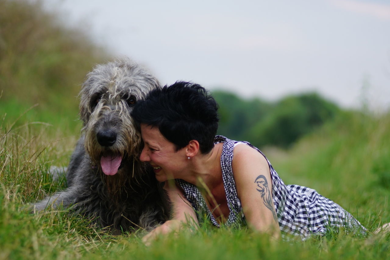 Happy woman lying by irish wolfhound on grassy field