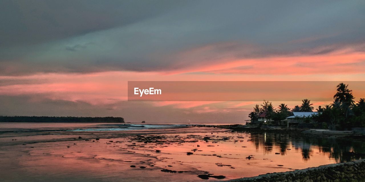 Scenic view of beach against dramatic sky during sunset