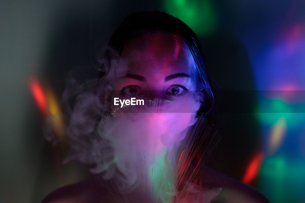 Close-up portrait of young woman holding multi colored fiber optic and smoke