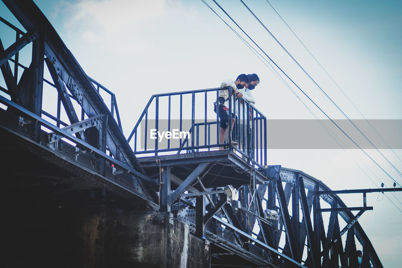 sky, bridge, architecture, blue, nature, one person, railing, low angle view, built structure, water, transportation, day, adult, men, outdoors, cloud, full length, transport, occupation, hat