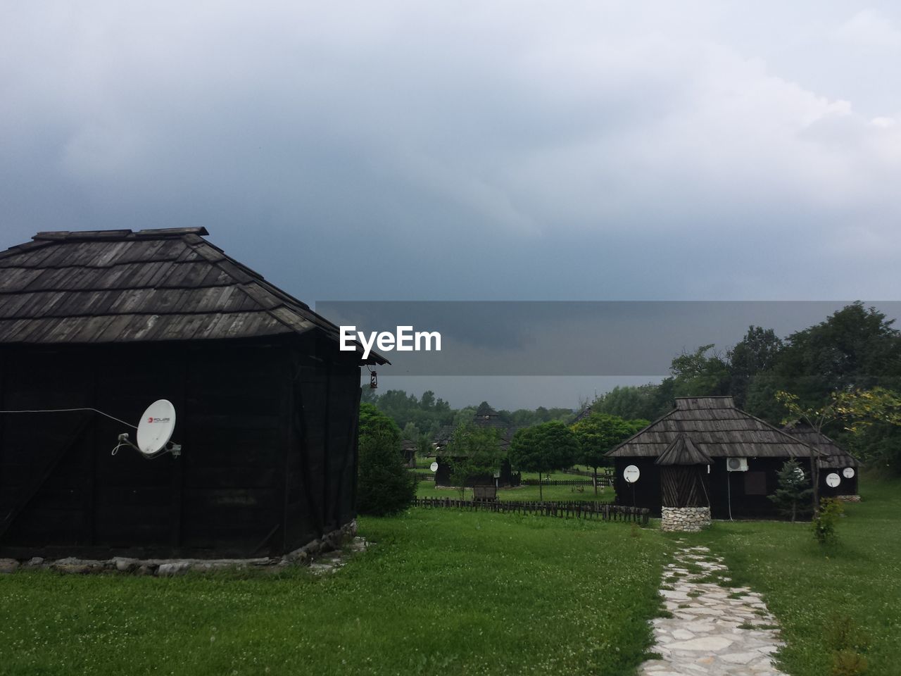 HOUSES ON GRASSY FIELD AGAINST CLOUDY SKY