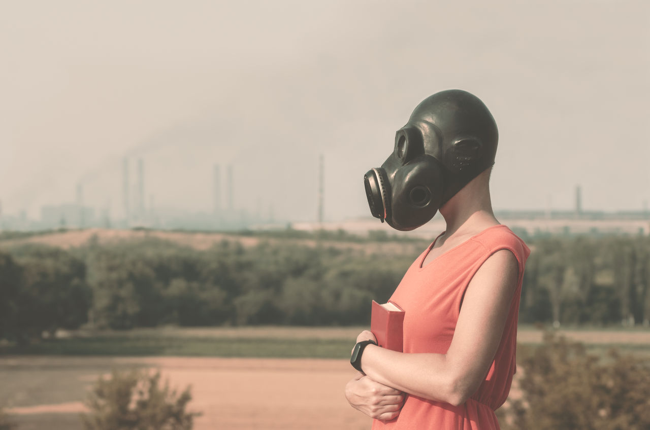 Woman wearing gas mask holding book while standing outdoors