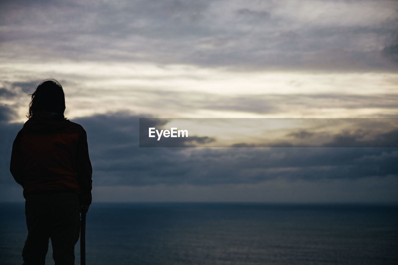 Rear view of woman looking at sea against cloudy sky