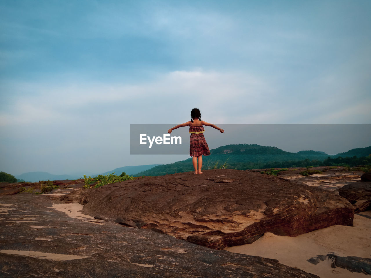 REAR VIEW OF MAN STANDING ON ROCK AT BEACH AGAINST SKY