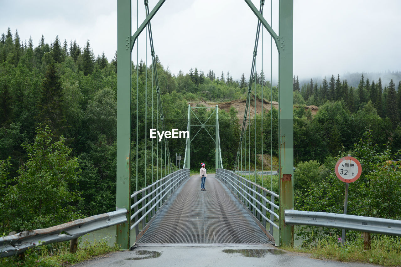 Full length of woman standing on bridge at forest