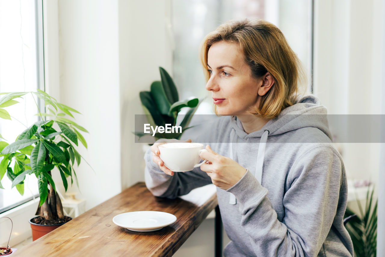 Woman looking away while holding coffee cup on table