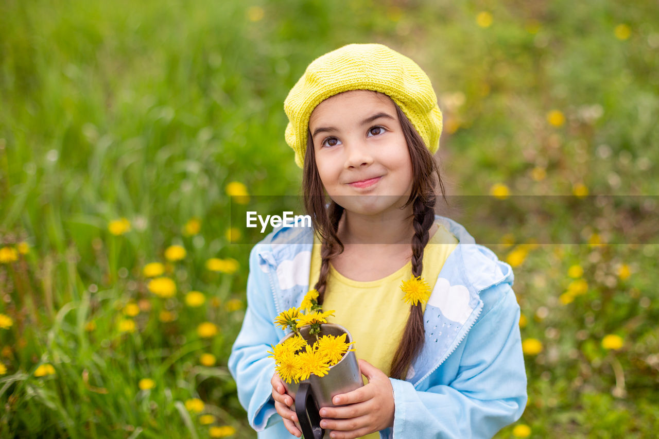 Portrait of a  little girl with two pigtails holds a bouquet of yellow dandelions in a mug, looks up