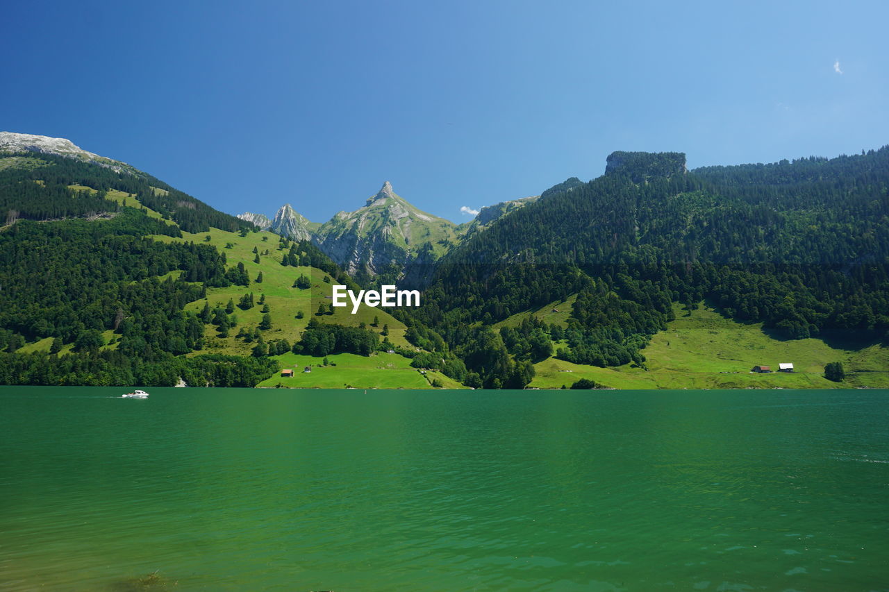 Scenic view of lake and mountains against clear blue sky