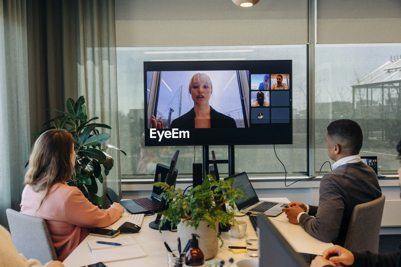 Colleagues doing video conference with businesswoman over tv screen at office