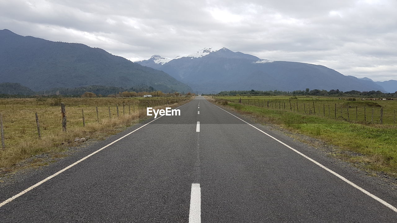 Empty road leading towards mountains against sky