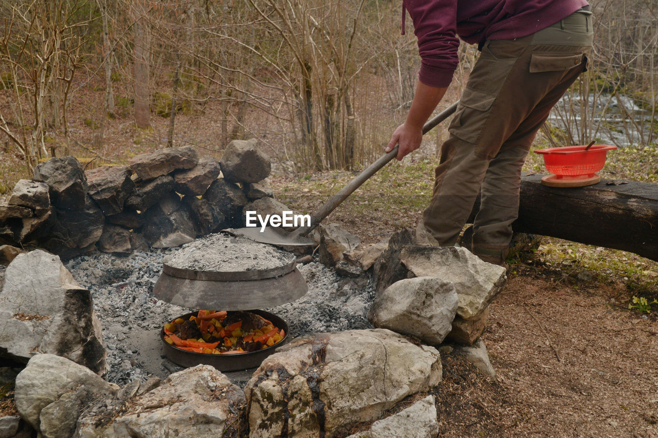 Low section of man with shovel preparing food on bonfire