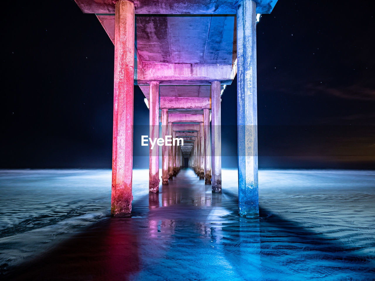 Blue and red lit underside of pier with night sky