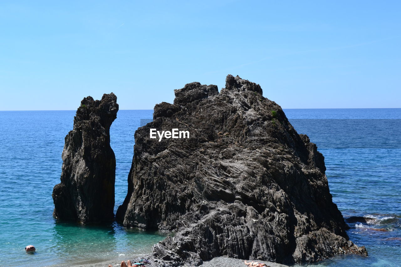 Rock formation in sea against clear blue sky