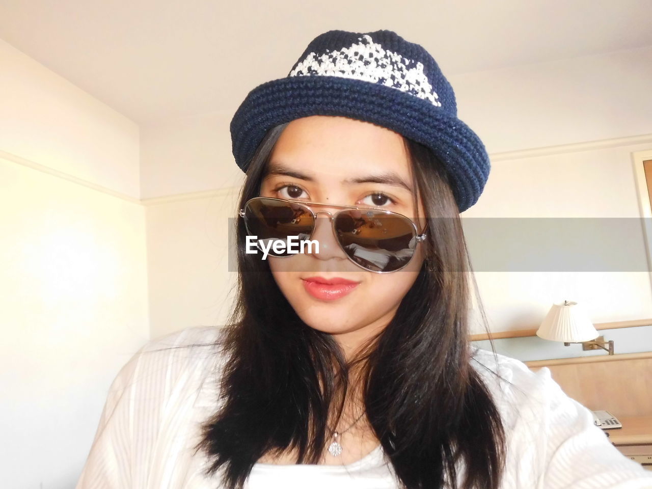 Portrait of young woman wearing sunglasses and hat at home