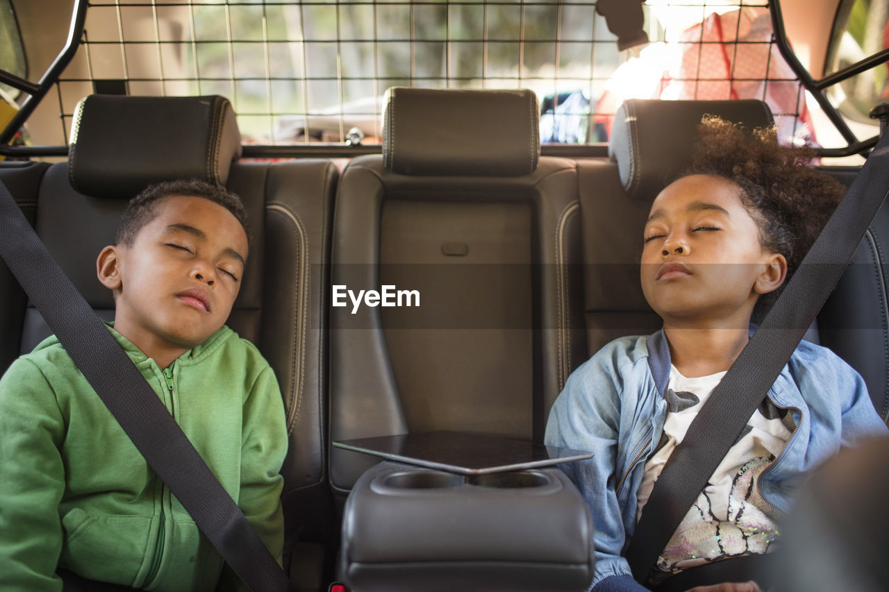 Tired siblings sleeping in electric car