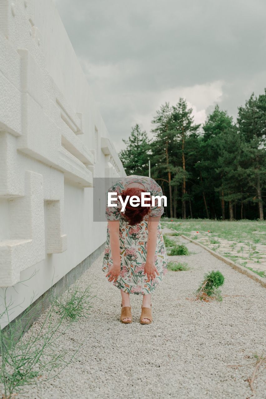 REAR VIEW OF WOMAN STANDING BY WALL AGAINST SKY