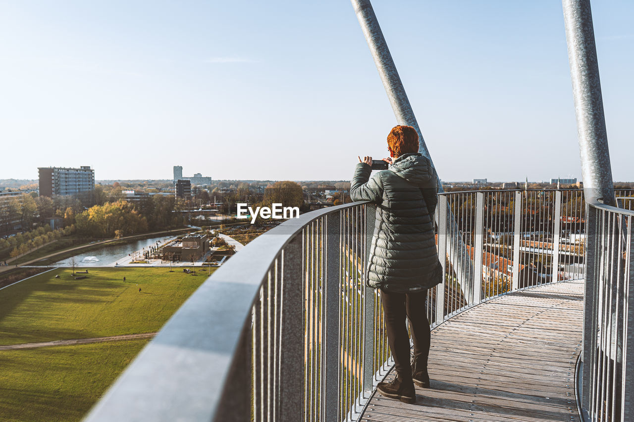 REAR VIEW OF WOMAN STANDING ON BRIDGE