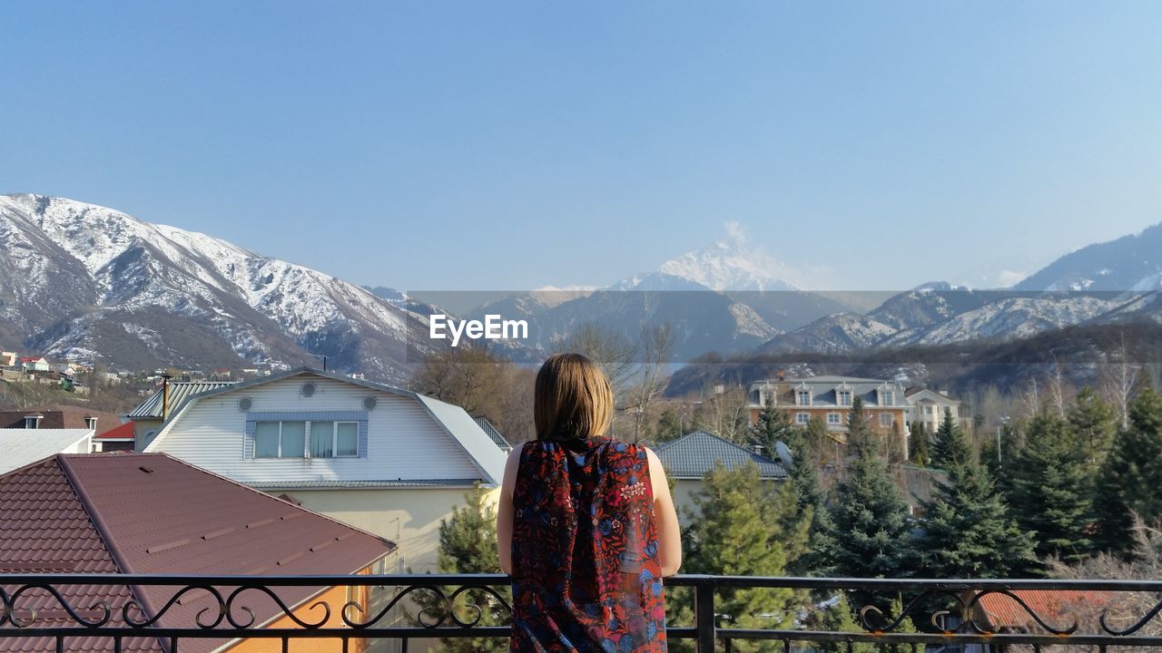 REAR VIEW OF WOMAN STANDING BY SNOWCAPPED MOUNTAIN