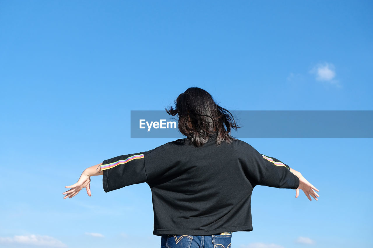 Rear view of woman standing against blue sky