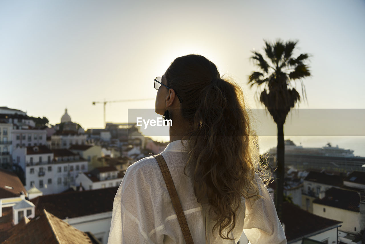 Young woman standing on rooftop in city during sunset