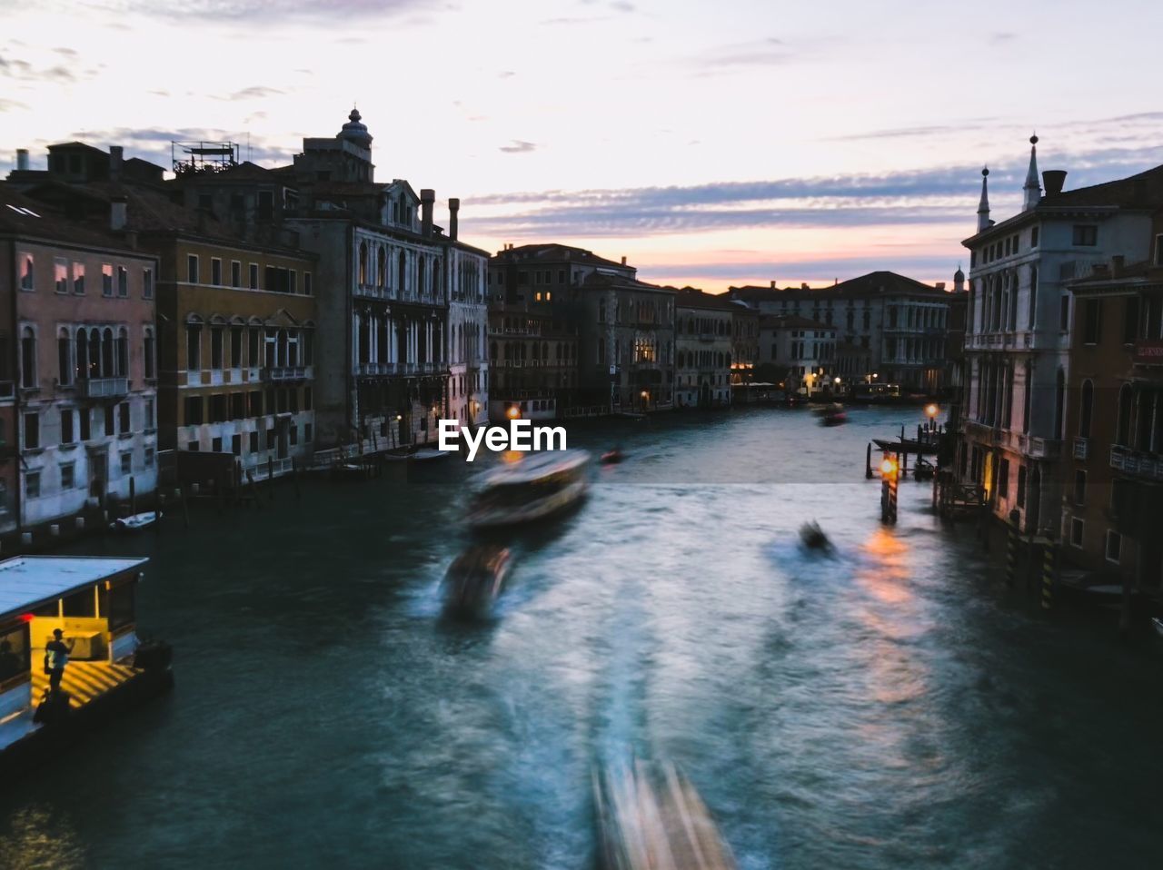 Canal amidst buildings in city against sky during sunset