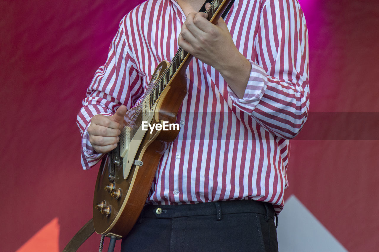 Midsection of man playing guitar against red wall