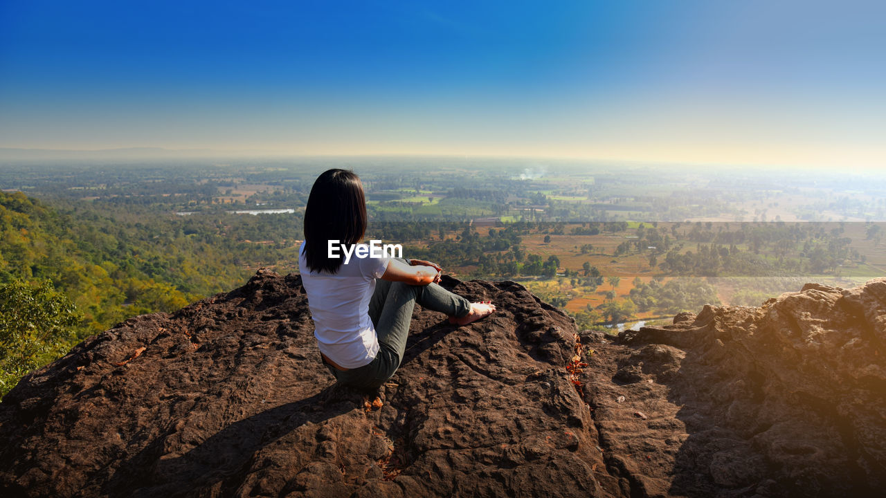 A  woman is sitting on an unusual rock on a mountain overlooking forest