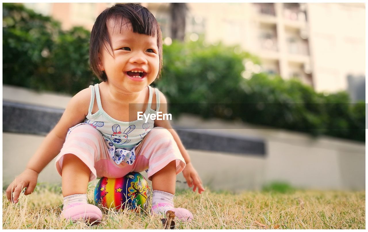 Cheerful girl sitting on ball over field at park