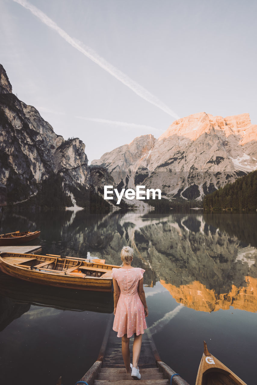 REAR VIEW OF WOMAN STANDING ON LAKE AGAINST MOUNTAINS