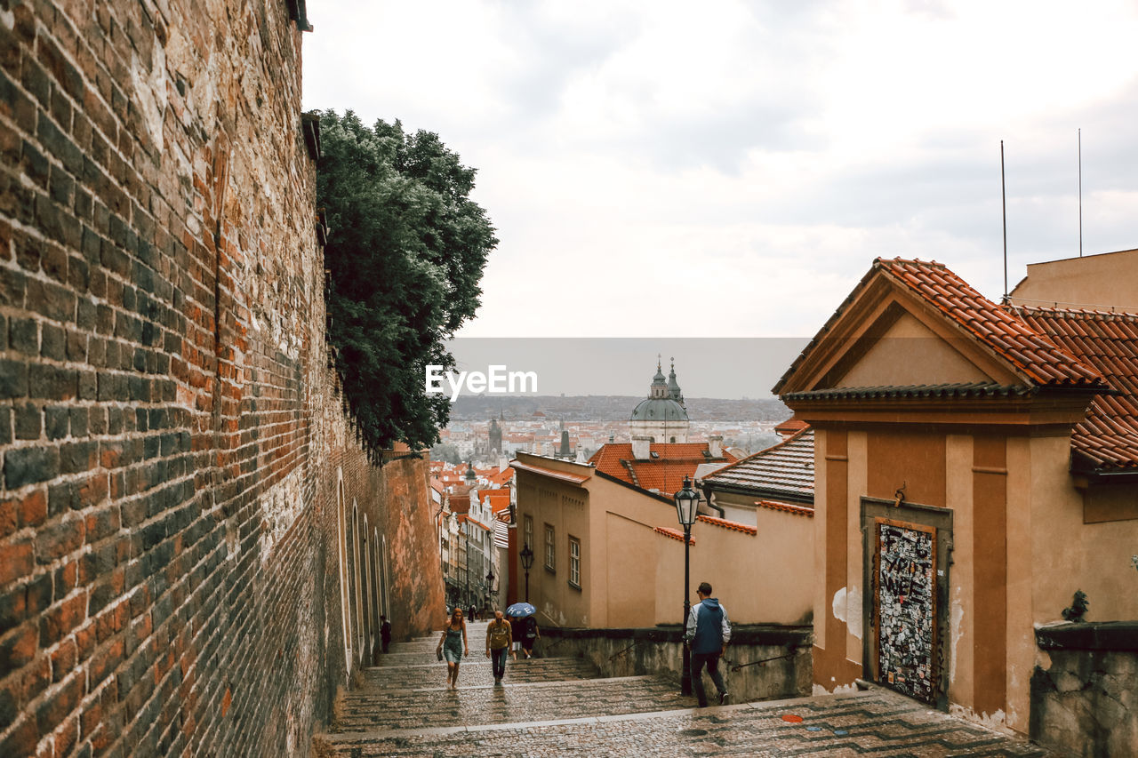 REAR VIEW OF PEOPLE WALKING IN ALLEY AMIDST BUILDINGS