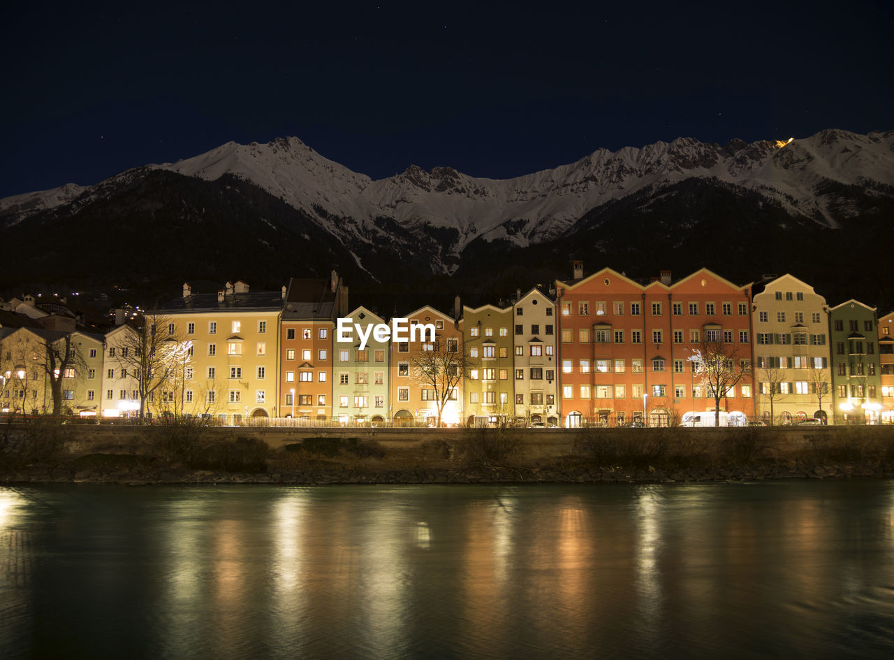 Illuminated buildings by mountains against sky at night