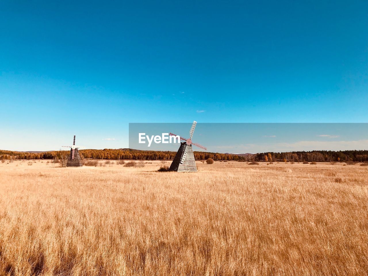 Traditional windmills on field against clear blue sky