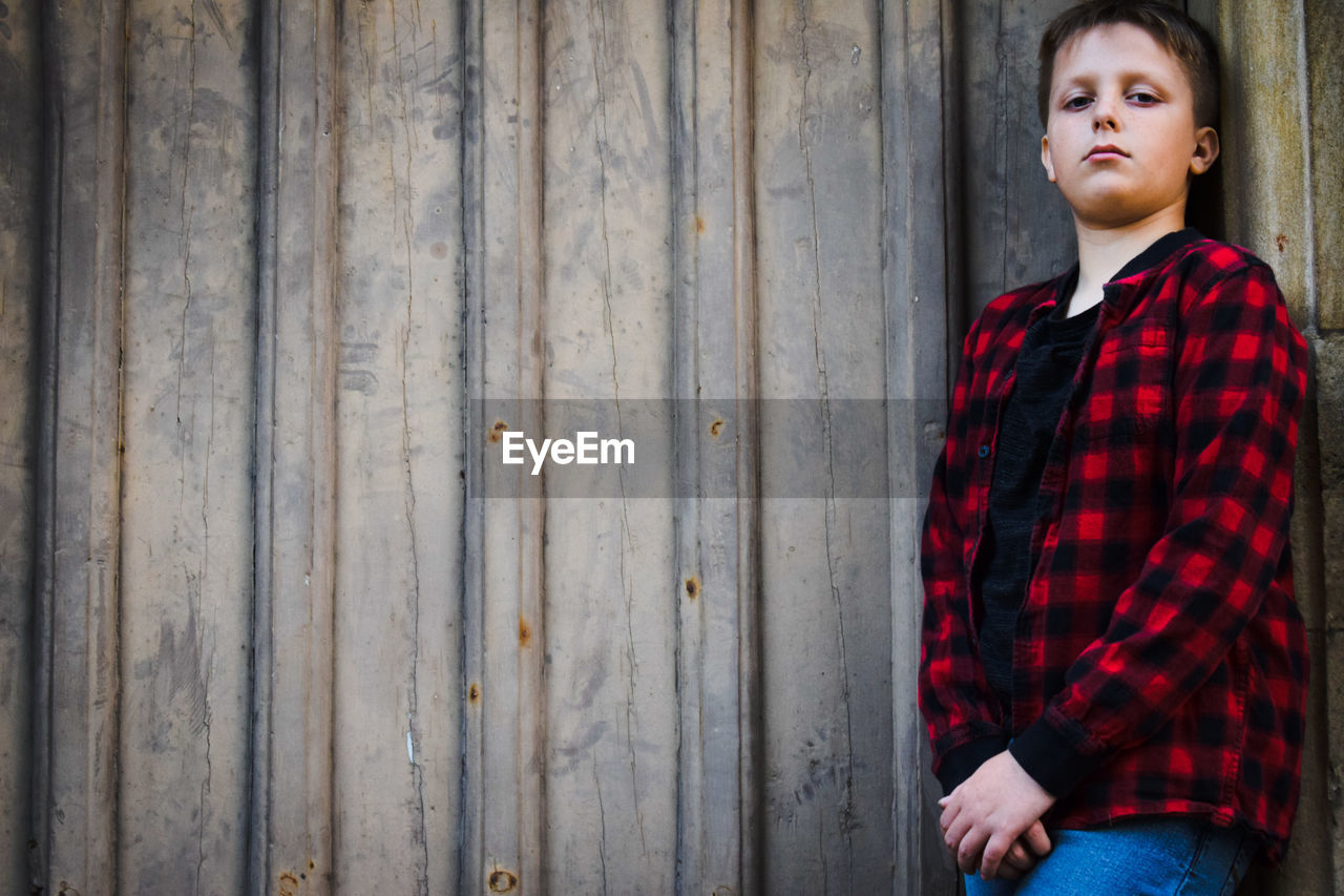 PORTRAIT OF TEENAGE BOY STANDING AGAINST WALL