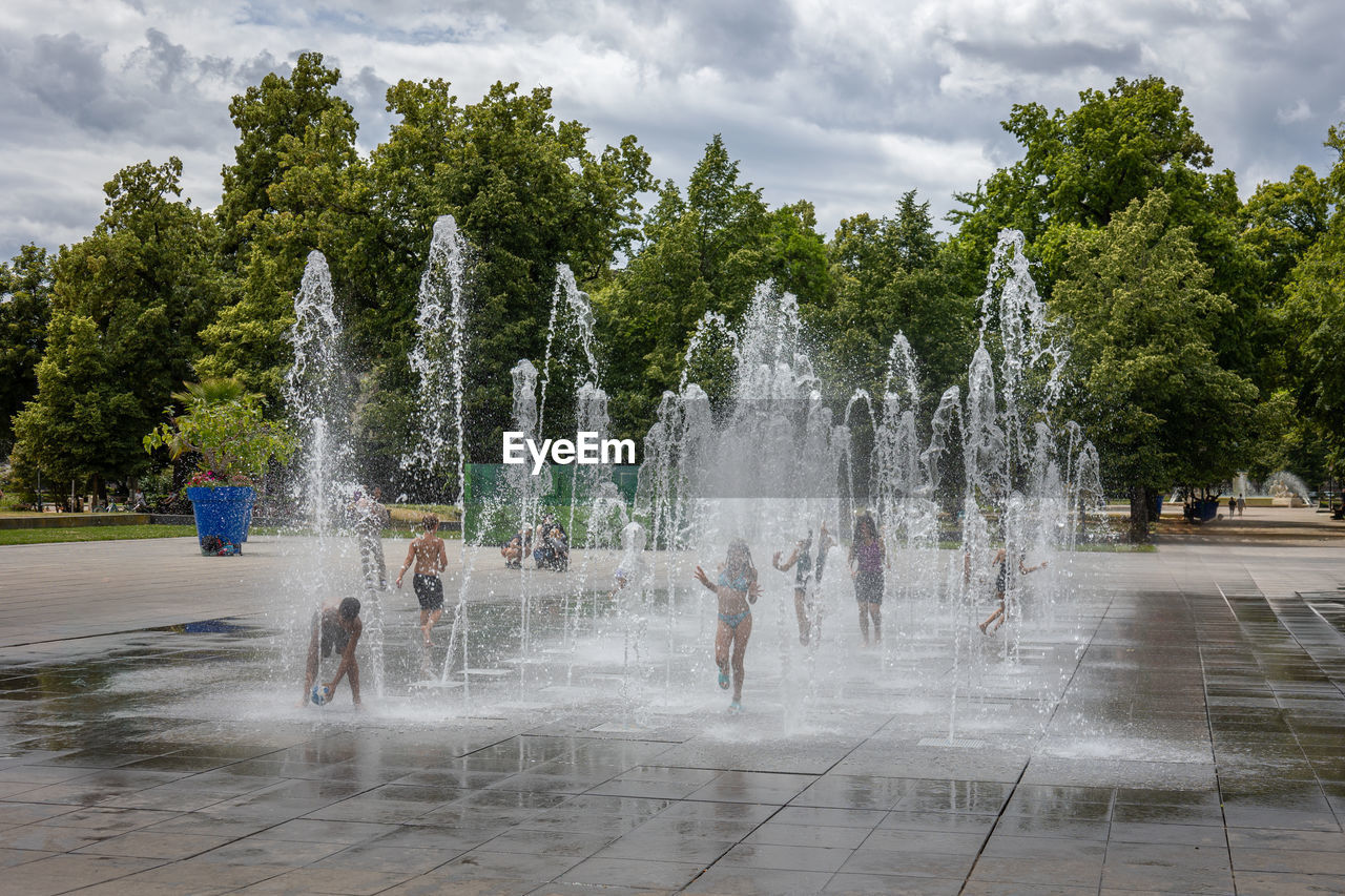fountain, water, water feature, tree, spraying, cloud, plant, nature, splashing, motion, sky, park, architecture, group of people, day, outdoors, town square, wet, travel destinations, travel, city, tourism