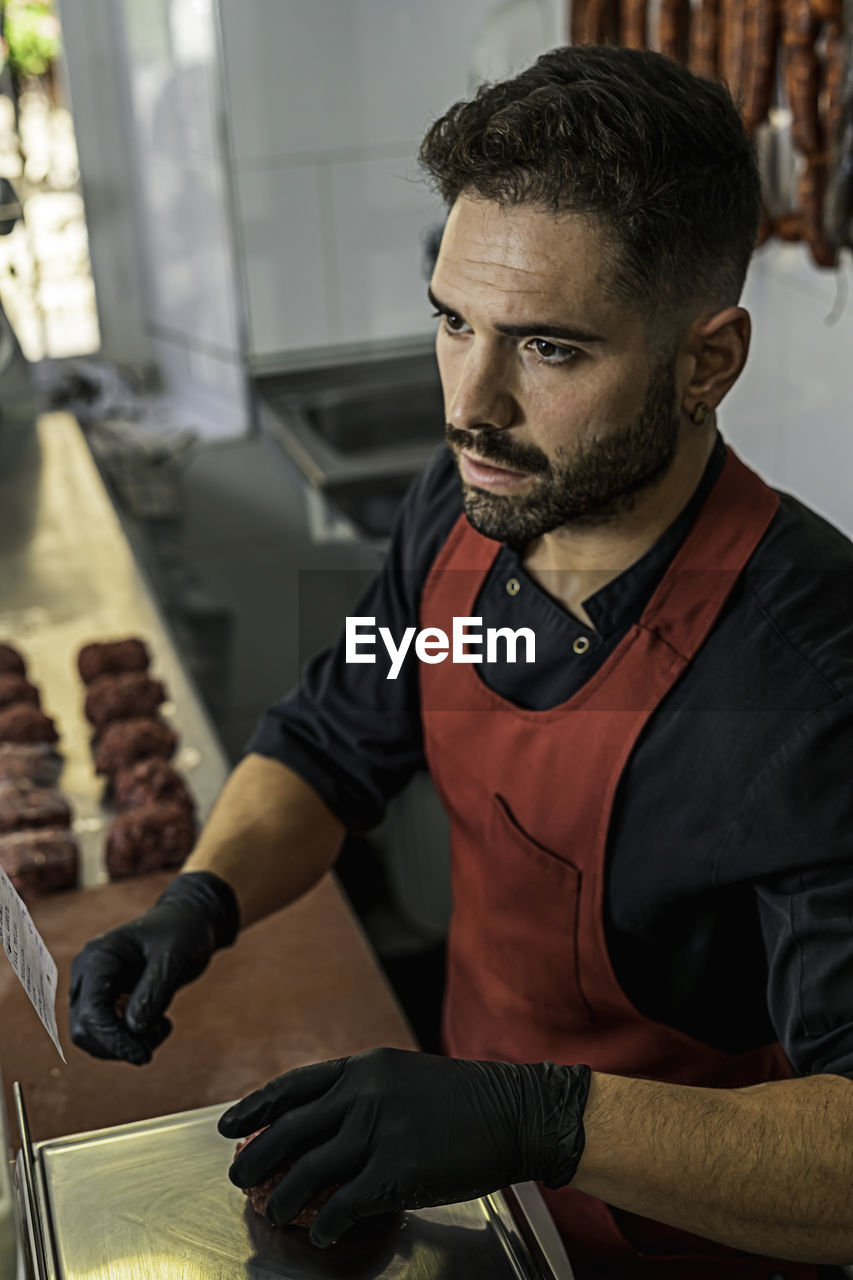 Butcher making raw beef burgers in butchers shop.