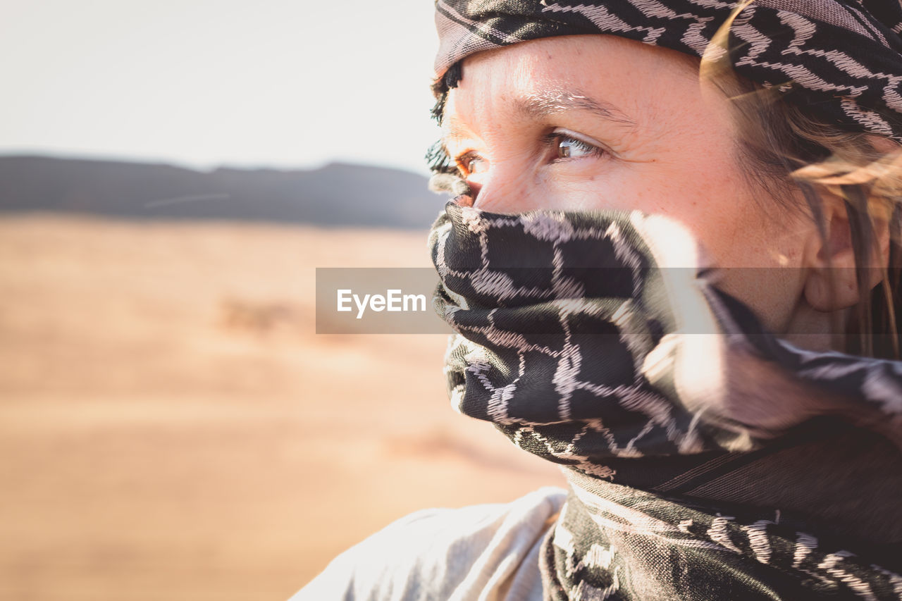 Close-up of woman covering face with scarf in desert against sky
